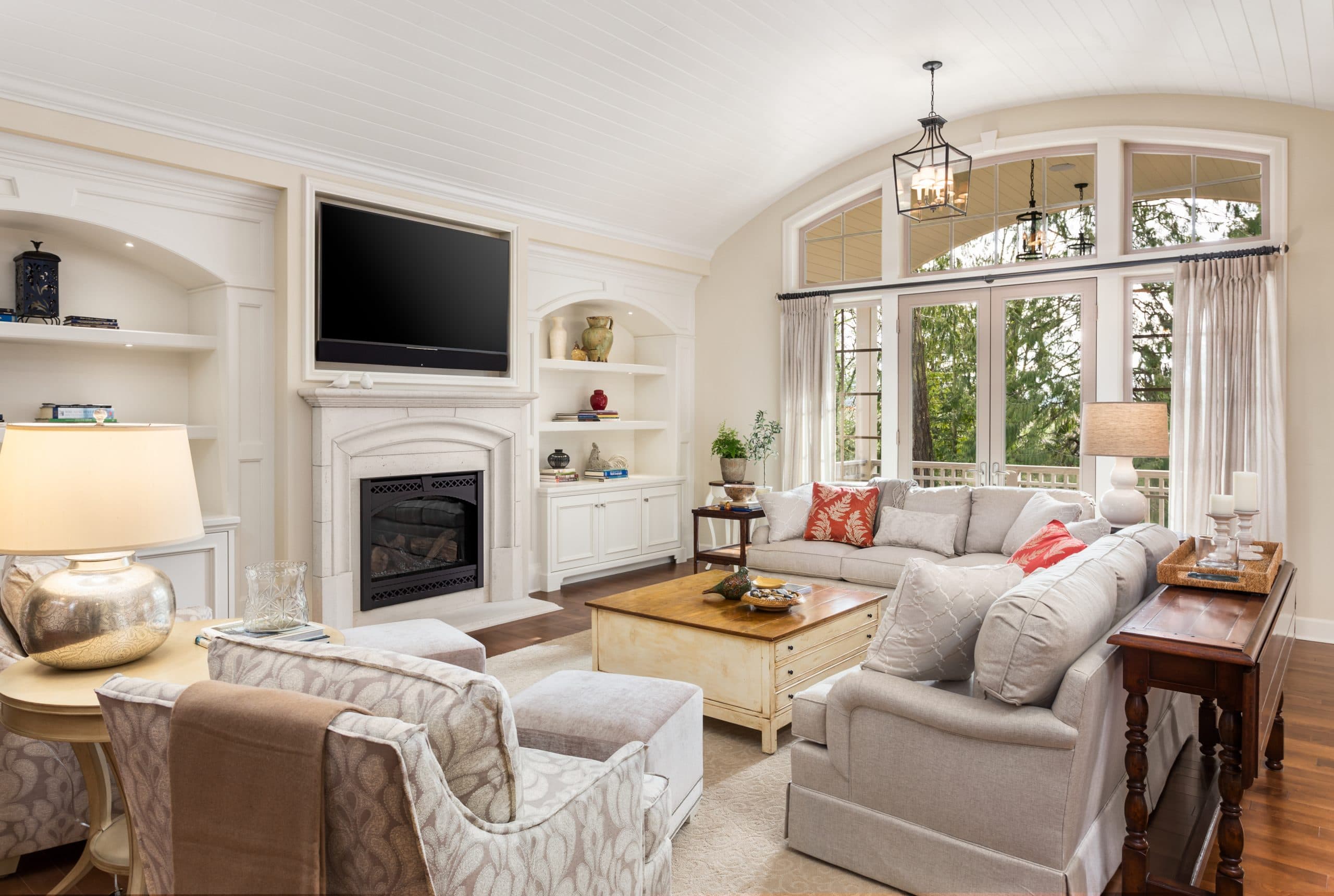 Beautiful living room in new traditional style luxury home. Features vaulted ceilings, fireplace with wall mounted tv, french doors leading outside, and elegant furnishings.