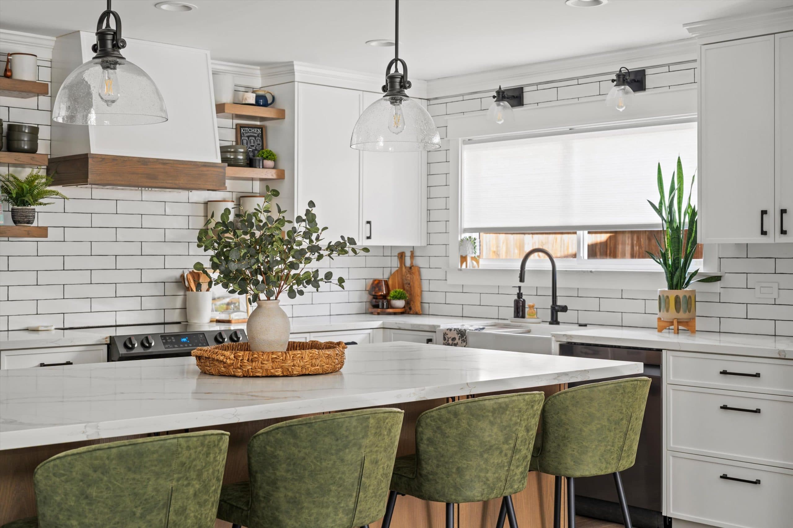 Kitchen island with white quartz waterfall countertop and natural wood base, green upholstered bar stools, subway tile backsplash, and floating wood shelves with styled decor