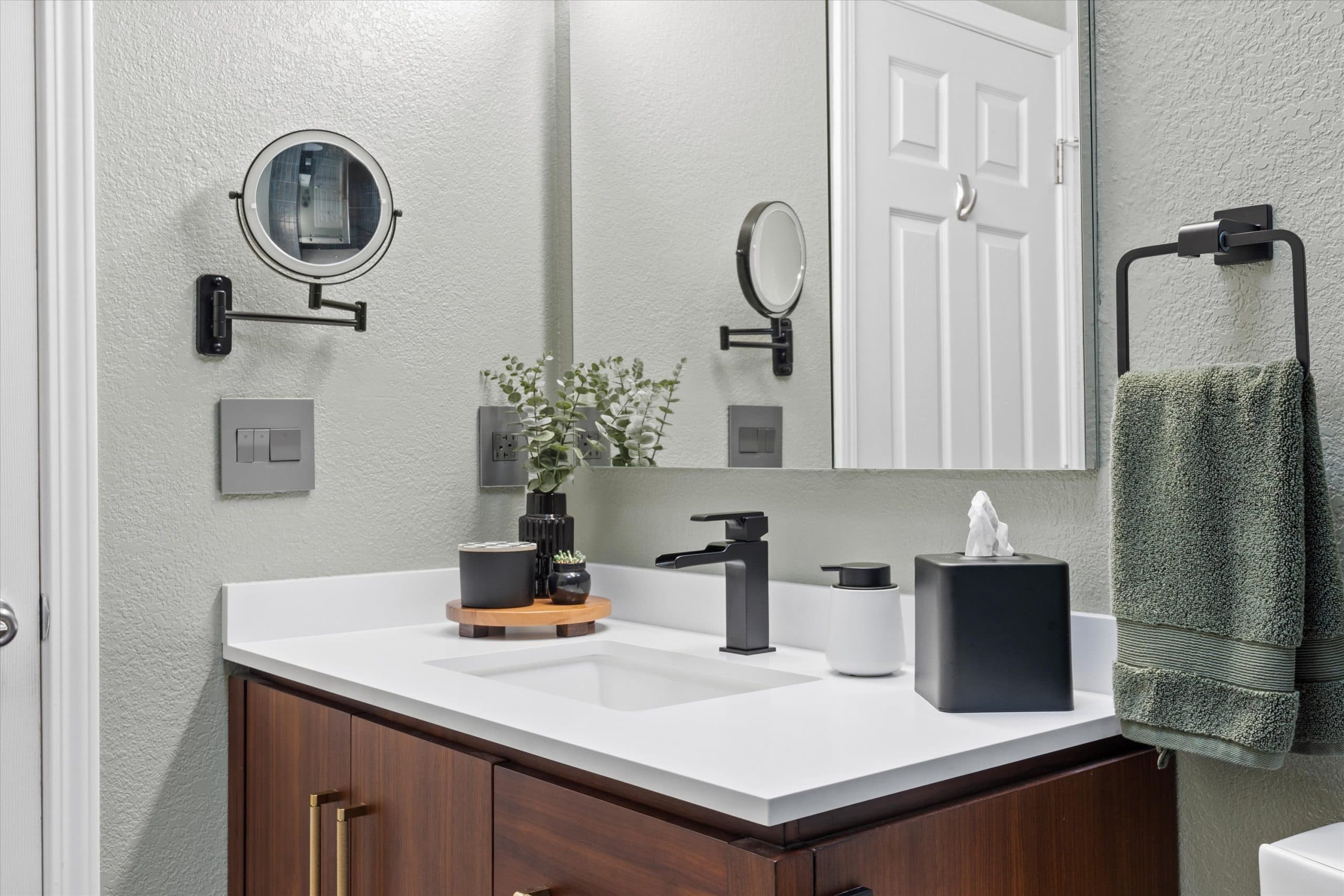 Bathroom vanity detail with white quartz countertop, warm wood cabinetry, matte black faucet, and round tilt mirror