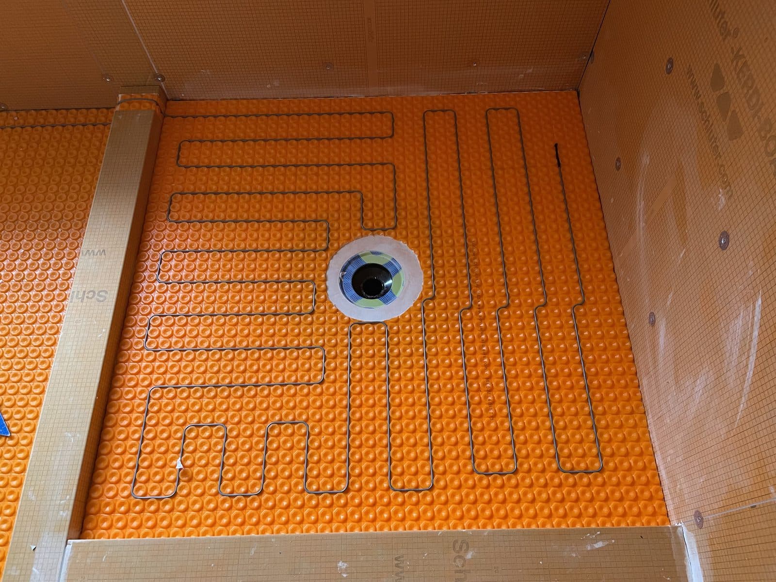 Schluter DITRA-HEAT membrane installed on a bathroom floor with the heating cable laid in a serpentine pattern around the drain, before tile goes down.