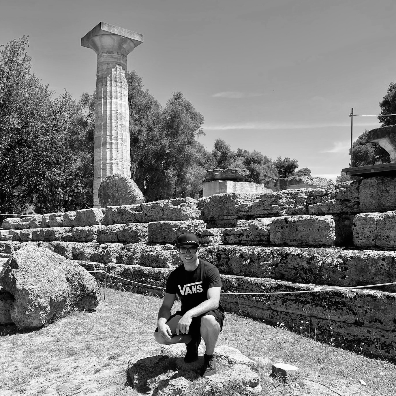 Garrett Parrish, owner of Parrish Construction Inc, sits on a rock next to an ancient column, embodying a blend of history and nature.